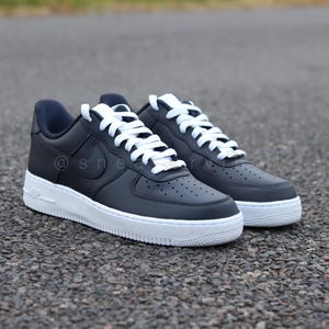 May include: A pair of black leather low-top sneakers with white laces and a white sole. The sneakers have a Nike swoosh logo on the side.