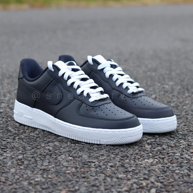 May include: A pair of black leather low-top sneakers with white laces and a white sole. The sneakers have a Nike swoosh logo on the side.