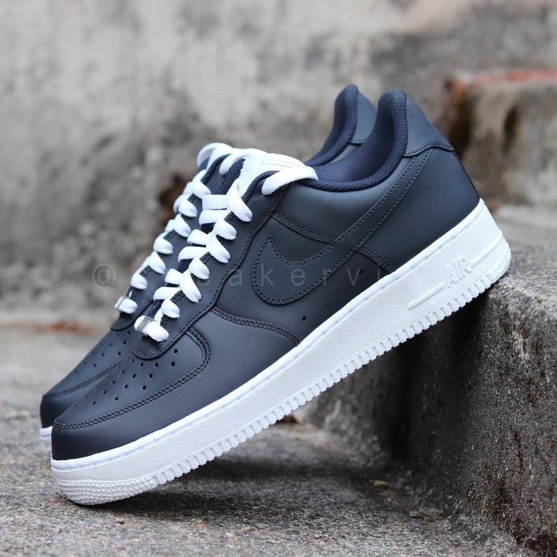 May include: Navy blue leather low-top sneakers with white laces and a white sole. The Nike swoosh logo is visible on the side of the shoe.
