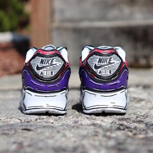 Puede incluir: Vista trasera de un par de zapatillas Nike Air Max 90. Las zapatillas tienen una base blanca con detalles morados y rojos. El logotipo de Nike y "AIR" son visibles en el tal&oacute;n. Contornos negros dan un aspecto de dibujos animados.