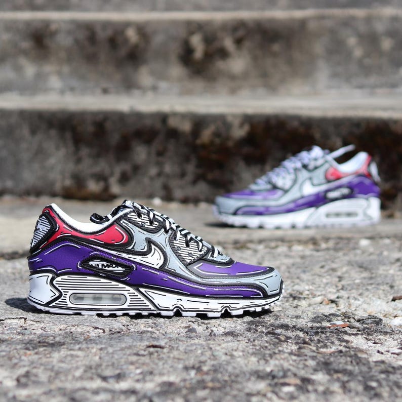 Puede incluir: Dos zapatillas Nike Air Max 90, una enfocada, la otra borrosa en el fondo. Las zapatillas presentan una combinaci&oacute;n de colores p&uacute;rpura, gris, rojo y blanco con contornos negros, creando un efecto de dibujos animados. Los zapatos est&aacute;n sobre una superficie de hormig&oacute;n.