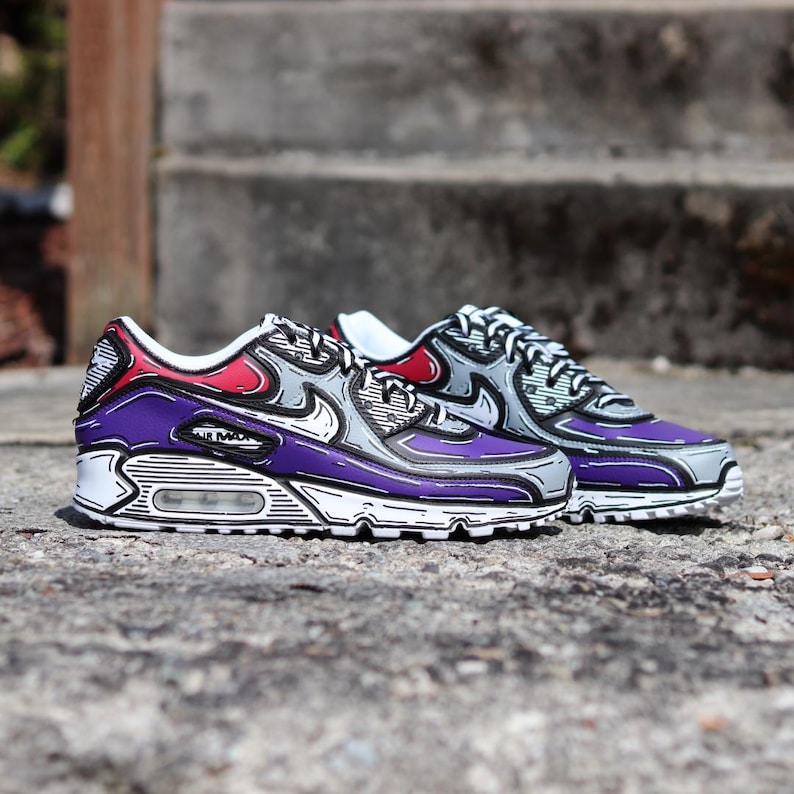 Puede incluir: Par de zapatillas Air Max 90 con un estilo de dibujos animados &uacute;nico. Los zapatos presentan una combinaci&oacute;n de colores p&uacute;rpura, gris, rojo y blanco con contornos negros. El dise&ntilde;o incluye el logotipo "Air Max" en el lateral.