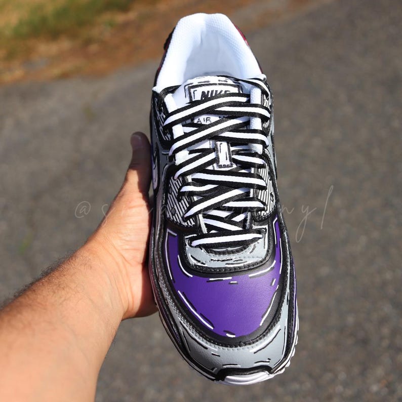 Puede incluir: Zapatilla Nike Air Max 90 personalizada con un dise&ntilde;o de estilo caricatura. El calzado presenta una combinaci&oacute;n de colores gris, negro y blanco, con detalles en morado en la puntera. Cordones blancos y leng&uuml;eta blanca. La zapatilla es sostenida por una mano.