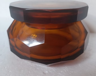 May include: A brown glass jar with a faceted lid. The jar has a geometric shape and is made of clear glass.