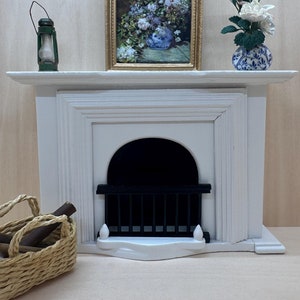May include: A white painted miniature fireplace with a black metal grate, a framed floral painting, a green lantern, and a white flower arrangement in a blue and white vase.