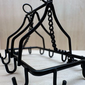 May include: Black metal hanging rack with multiple hooks and a chain. The rack is designed to hold mugs, cups, or other kitchen items.
