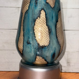 May include: A teal and gold glitter tumbler with a snake skin pattern. The tumbler is on a rotating base.