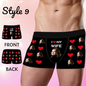 Peut inclure: Caleçon noir avec un motif répétitif de cœurs rouges et le visage d'une femme, accompagné du texte I LOVE MY WIFE imprimé en blanc. Le modèle présente une large ceinture noire et est illustré sous des angles avant et arrière.