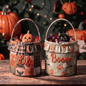 May include: Two cylindrical fabric Halloween buckets with handles. The left bucket features a patchwork pattern with a pumpkin, bat, and the name Lily. The right bucket has a light green background with ghosts, pumpkins, and the name Boone.