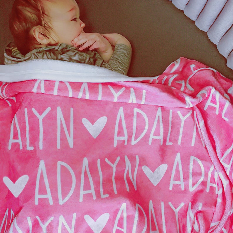 May include: A pink baby blanket with the name "Adalyn" repeated in white lettering and hearts.
