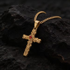 Könnte beinhalten: Goldfarbene Kreuz-Anhänger-Halskette mit einem roten Edelstein in der Mitte. Das Kreuz weist ein verziertes Blumendesign auf und hängt an einer passenden Goldkette. Der Anhänger wird vor einem dunklen, strukturierten Hintergrund präsentiert.