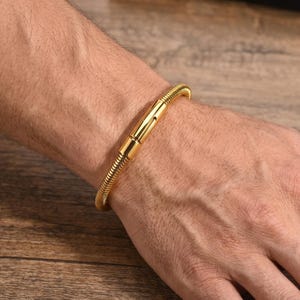 Può includere: Un braccialetto dorato con un design a catena a serpente. Il braccialetto ha una chiusura magnetica e viene indossato al polso. Il braccialetto è in metallo ed è un gioiello.