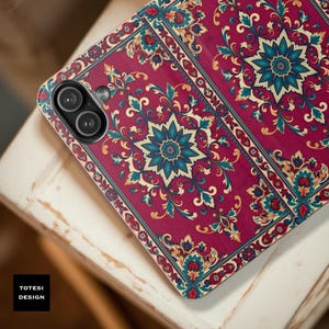 May include: A phone case with a burgundy floral pattern. The design features teal and cream-colored floral accents and a central starburst motif. The case has a camera module with two lenses and the text "TOTESI DESIGN".
