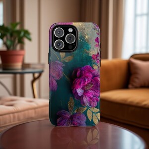 May include: A teal and gold phone case with a floral design featuring pink and purple flowers. The case has a cutout for the camera lens.