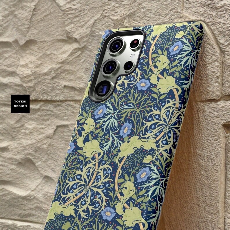 Pu&ograve; includere: Una custodia per telefono blu con un motivo floreale in tonalit&agrave; di verde, giallo e blu. La custodia ha un ritaglio per l'obiettivo della fotocamera.