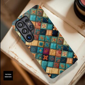 May include: A patterned phone case featuring a patchwork design in shades of teal, blue, orange, and gold. The case has a camera module with multiple lenses. The text "TOTESI DESIGN" is visible in the lower left corner.