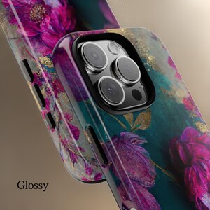 May include: A glossy phone case with a floral design featuring pink and purple flowers on a teal background with gold accents. The case has a raised camera bump with a black border.
