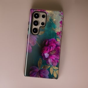 May include: A phone case with a floral design. The case features a dark green background with pink and purple flowers and gold accents.