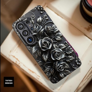 May include: Black phone case with a raised floral design featuring roses and leaves. The case has a textured appearance and a camera cutout. The brand name "TOTESI DESIGN" is printed on the lower left corner.