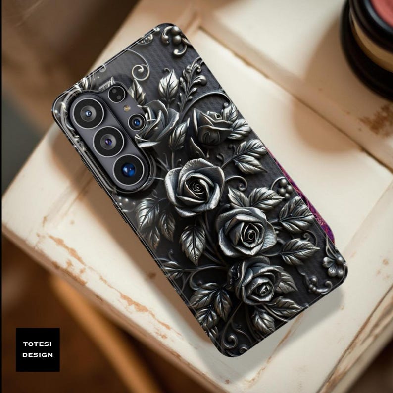 May include: Black phone case with a raised floral design featuring roses and leaves. The case has a textured appearance and a camera cutout. The brand name "TOTESI DESIGN" is printed on the lower left corner.