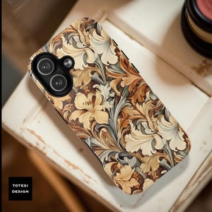 May include: A phone case featuring a floral design in shades of beige, brown, and gray. The case has a black border and a dual-lens camera cutout. The text "TOTESI DESIGN" is in a black box in the lower left corner.