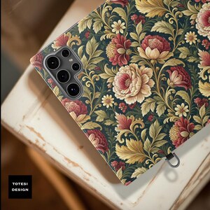 May include: A phone case with a floral pattern featuring large, cream and red flowers, yellow accents, and green leaves on a dark teal background. The case has a camera cutout and a small metal loop. The text "TOTESI DESIGN" is in the lower left corner.