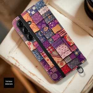 May include: A multi-colored phone case with a patchwork design. The case features a variety of patterns in shades of purple, blue, red, and orange. A black elastic band secures the case, and the text "TOTESI DESIGN" is visible.