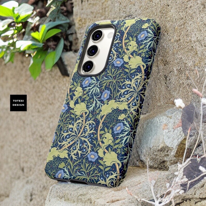 Pu&ograve; includere: Una custodia per telefono blu e verde con un motivo floreale. La custodia ha un ritaglio per l'obiettivo della fotocamera e un bordo rialzato attorno ai bordi per proteggere lo schermo.