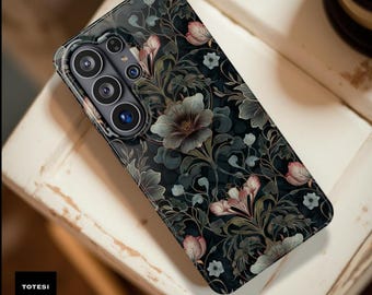 May include: A smartphone case with a dark floral pattern featuring pink, gray, and white flowers on a black background. The case has a glossy finish and a camera module with multiple lenses. The text "TOTESI DESIGN" is in a black box.