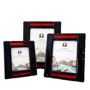 May include: Three black picture frames with a red stripe accent. Each frame has a white interior with a scenic image of a European city. The frames are square and have the text "Vetro di Murano".
