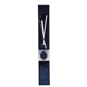 May include: A long, rectangular wall clock with a black finish and white clock hands. The clock has a decorative design with a central, textured, teardrop-shaped element. The clock face has a simple, minimalist design.