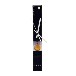 May include: A modern, rectangular wall clock with a black face and white hands. The clock features a gold-coloured, teardrop-shaped accent and small, colourful decorative elements. The clock's dimensions are approximately 51 cm in height.