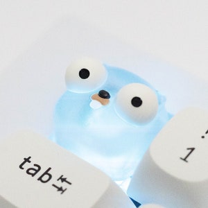 Könnte beinhalten: Eine blaue und weiße Tastatur-Tastenkappe mit einem Cartoon-Gopher-Design. Der Gopher hat große Augen und einen kleinen Mund. Die Tastenkappe ist mit "tab" beschriftet.