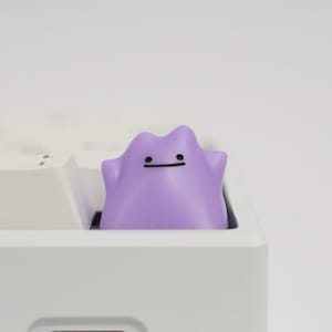 Peut inclure: Un capuchon de touche de clavier violet avec un visage simple, conçu pour s'adapter à un clavier mécanique.
