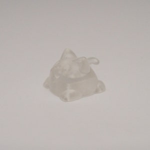 May include: A clear, translucent plastic figurine of a small, cartoon-like creature with a pointed head and a tail. The figurine is about 2 inches tall and has a slightly textured surface.