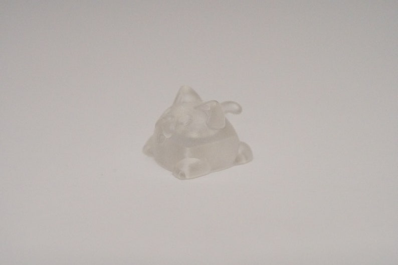 May include: A clear, translucent plastic figurine of a small, cartoon-like creature with a pointed head and a tail. The figurine is about 2 inches tall and has a slightly textured surface.