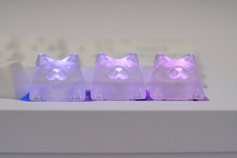May include: Three small, translucent, purple cat-shaped figurines with glowing eyes. The figurines are arranged in a row on a white surface.