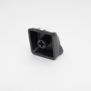 May include: A black plastic keyboard keycap with a plus sign on the top. The keycap has a white border around the edge.