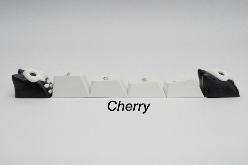 May include: Five white keyboard keycaps with black and white skull keycaps on either end. The keycaps are labeled "ESC", "F1", "F2", "F3", and "F4". The text "Cherry" is printed below the keycaps.