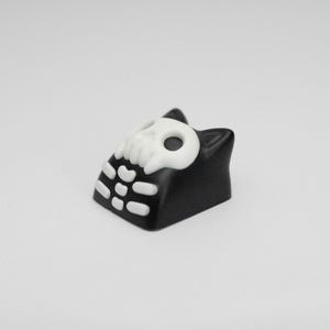 May include: Black and white keycap with a skull design and a cat-like shape.