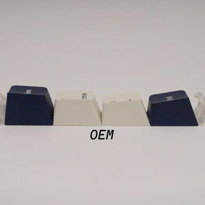 May include: Four keycaps, two white and two dark blue, with the word "OEM" printed below them. The keycaps are flanked by two clear plastic keycap pullers.