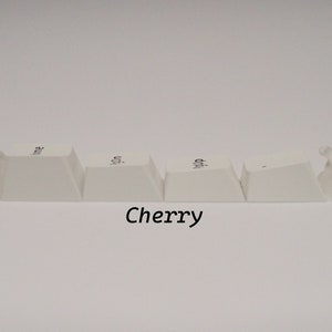 May include: Five white keycaps with a clear plastic keycap on each end. The keycaps have the word "Cherry" printed on them.