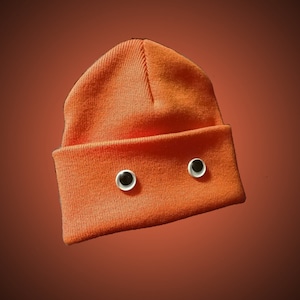 May include: An orange beanie with two white googly eyes sewn on the front.