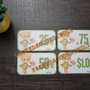 May include: Four rectangular price tags with a green border and a cartoon bear holding flowers. The tags display prices of 25¢, 50¢, 75¢, and $1.00. The text "PACKEDACCORDINGLY" is stamped across the tags.