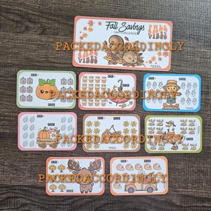 May include: A collection of nine rectangular savings challenge cards featuring autumn-themed illustrations including a squirrel, pumpkin, scarecrow, wagon, flowers, goose, moose, and truck. Each card displays the text "EACH" and "SAVED" with icons.