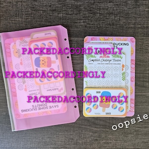 May include: A pink translucent binder pouch containing several printed paper challenge trackers with donut and popsicle illustrations, alongside a stack of loose challenge tracker cards featuring similar colorful food graphics and text.