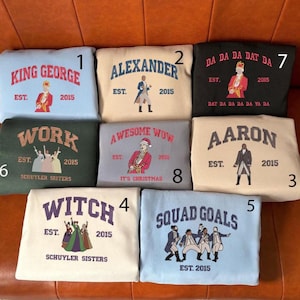 Peut inclure: Collection de huit sweat-shirts avec différents motifs et textes. Les motifs incluent "King George", "Alexander", "Aaron", "Squad Goals", "Witch", "Work", "Da Da Da Dat Da" et "Awesome Wow". Chaque sweat-shirt a une couleur et un graphisme différents.