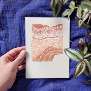 Peut inclure: Une impression d'art blanche représentant un paysage abstrait dans des tons orange et pêche. L'impression a un aspect texturé avec des traits détaillés, et le texte "Ecrits Mouvements de Surface" est imprimé verticalement à gauche.