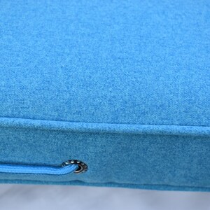 Puede incluir: Primer plano de un coj&iacute;n azul brillante con una tela texturizada. El coj&iacute;n tiene un detalle de cremallera con una arandela de color plateado. La tela parece ser un material suave similar al fieltro.