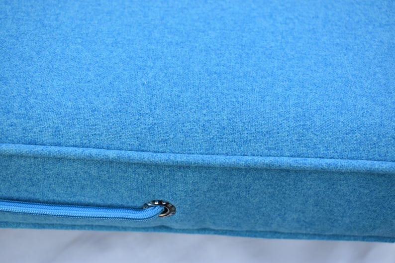 Puede incluir: Primer plano de un coj&iacute;n azul brillante con una tela texturizada. El coj&iacute;n tiene un detalle de cremallera con una arandela de color plateado. La tela parece ser un material suave similar al fieltro.